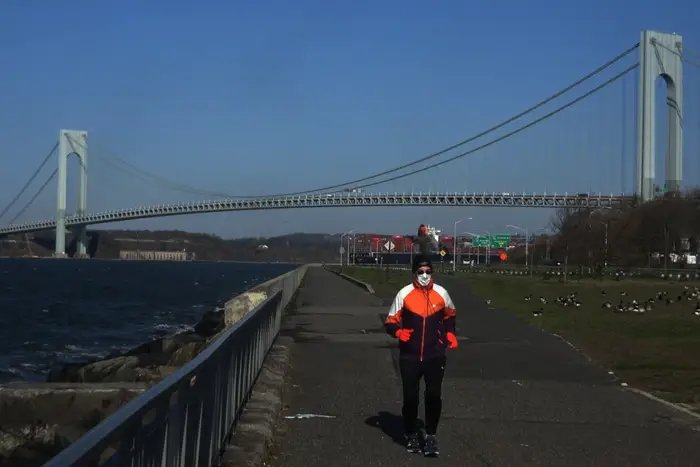 A photo of a man running in front of the Verrazano bridge